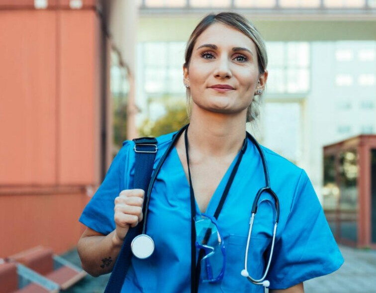 Nurse carrying a bag and stethoscope outside a building